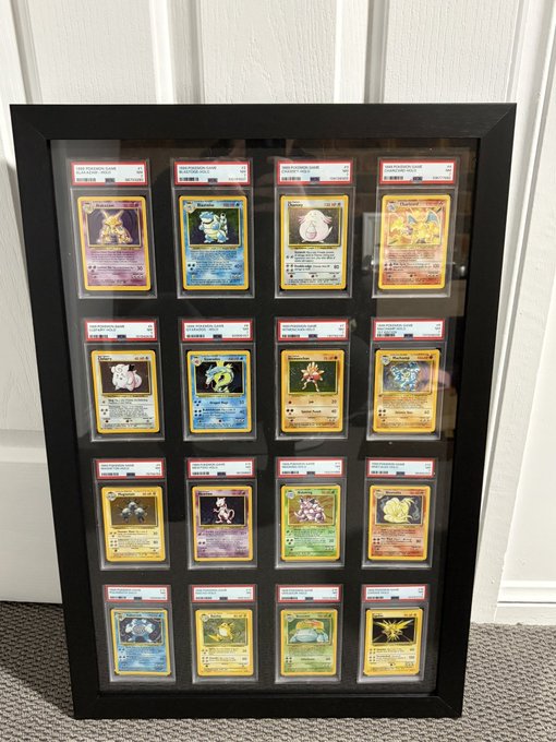 A black shadow box frame displaying a collection of 16 PSA-graded Pokémon cards arranged in a 4x4 grid, mounted on a wall.