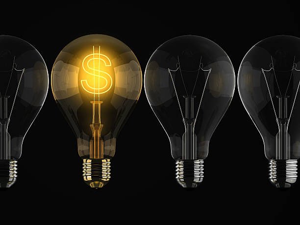 The image features a row of five light bulbs with one of them glowing brightly with a dollar sign in front of it. The remaining four bulbs are dark, creating a contrast between the illuminated bulb and its surroundings. The dollar sign in the middle of the row stands out as the most prominent element within the scene.