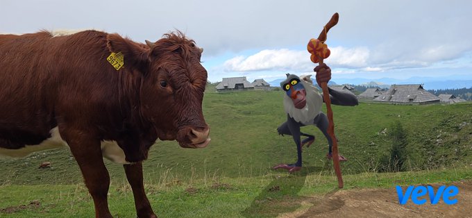 A brown cow with a yellow ear tag stands in a grassy field near a bird character holding a staff, with a 'veve' watermark in the bottom right corner.