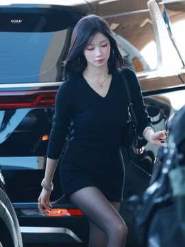 A young woman in a black long-sleeved mini dress steps out of a vehicle, carrying a black bag, with a 'GOLF' logo visible on the window.