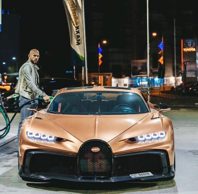 A man stands next to a copper/bronze-colored Bugatti hypercar at a nighttime gas station, with the Toyota logo visible in the background.