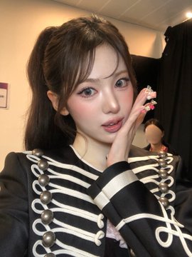 A selfie of a young woman with high pigtails and a military-style black jacket with white braiding and silver buttons.
