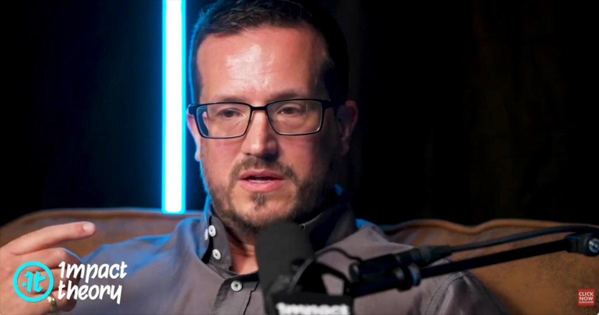 The image features a man wearing glasses, sitting down with his hand raised as if he's speaking or gesturing during an interview. The background of the image is dark, which contrasts with the bright blue neon strip that runs across the top left corner. This strip appears to be emitting a blue light, adding a unique visual element to the scene. The man and the neon strip are both located in the upper part of the image, while the rest of the photo is filled with black text.