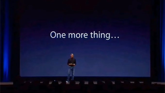 A presenter stands on stage in front of a large dark screen displaying "One more thing…" — a signature Apple keynote phrase, humorously appropriated here as a plea to reintroduce the Bitcoin emoji before the presentation ends.
