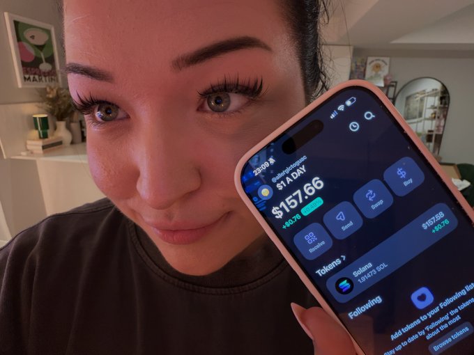 In the image, a woman is holding up her smartphone showing details about her stock trading account. She is smiling at the camera while demonstrating the information displayed on her phone screen. The account balance shown is $1.76, which indicates that she has purchased 1 share of a company for 192 cents. This amount corresponds to approximately $19.88. The woman also mentions that she will be continuing to spend more money in the coming days as she engages with her stock trading account on this app called Binance Trading Bot.