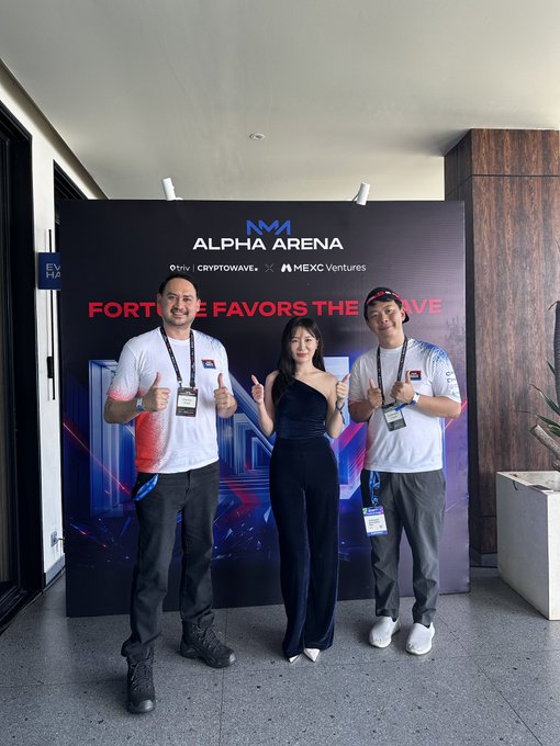 Three people posing with thumbs up in front of an 'ALPHA ARENA' event banner by CRYPTOWAVE and MEXC Ventures, with the text 'FORTUNE FAVORS THE BRAVE' displayed.