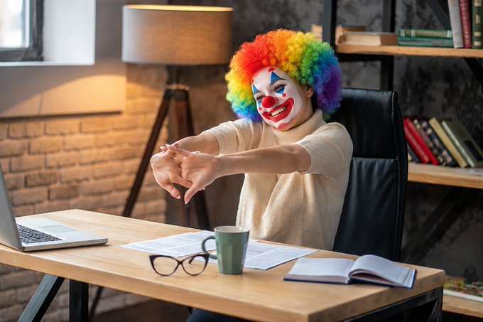 A person dressed as a clown sits at a desk, stretching their hands, ready to share their latest "key opinion" on Twitter dot com after a "Saylor" tweet.