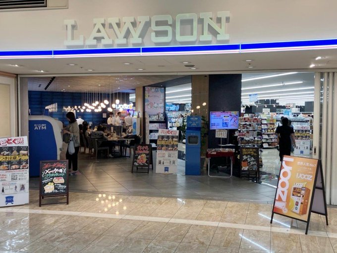 The entrance to a 'LAWSON' convenience store inside a building, featuring promotional displays and a café seating area.