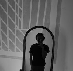 A black-and-white photograph of a person wearing headphones, taking a mirror selfie in an arched mirror.
