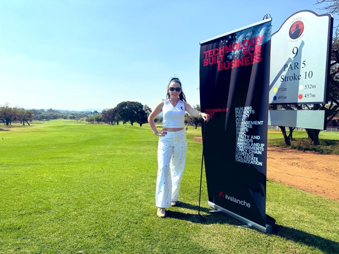 A woman in white pants and a white top stands beside an 'avalanche' branded banner reading 'TECHNOLOGY BUILT FOR BUSINESS' on a golf course near a hole 9 par 5 sign.