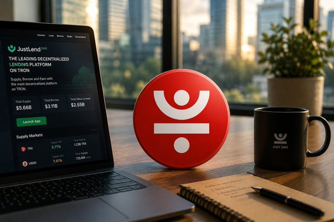 A laptop displaying the 'JustLend DAO' platform sits on a desk next to a large red Just DAO logo, a black branded mug, and a potted plant against a city skyline.