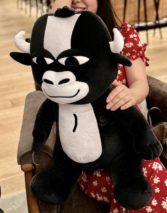 A person in a red floral dress smiles while holding a large black-and-white bull plush toy (Mumu the Bull) seated on their lap. The image showcases the giveaway prize alongside the festive 4th of July promotion offering $1000 in $ANSEM and $MUMU tokens.