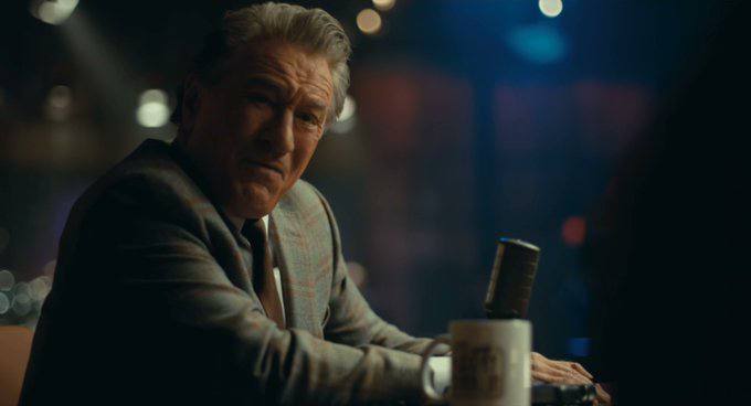 A distinguished man in a plaid suit sits at a bar holding a beer mug, his skeptical expression suggesting doubt—mirroring the post's tone, where someone named "Dip Wheeler" mockingly challenges a bear to reevaluate their stance after a purchase at a 50k market cap.