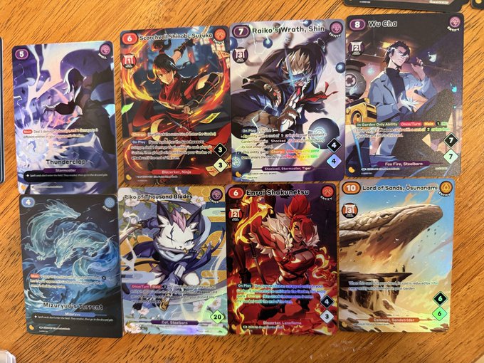 A collection of holographic Azuki TCG trading cards spread out on a wooden table, featuring rare pulls like "Thunderslip," "Mizuryuu, Kagonnau," "Mike of Thousand Blades," "Kaiza Shinobi, Susu" (numbered 6), "Raiko's Wrath, Shin" (numbered 7), "Barei, Shakunetsu" (numbered 6), "Wo Cho" (numbered 8), and the high-rarity "Lord of Sands, Osunagami" (numbered 10), showcasing the impressive results of opening their first Azuki TCG packs.