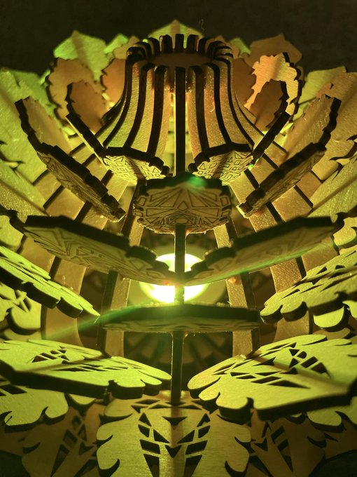 A close-up of an intricate wooden lantern or decorative structure illuminated from within, casting a greenish-yellow glow.