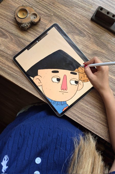 A photo of an artist using a stylus on a tablet to digitally draw a cartoon character with a black hat and long pink nose.