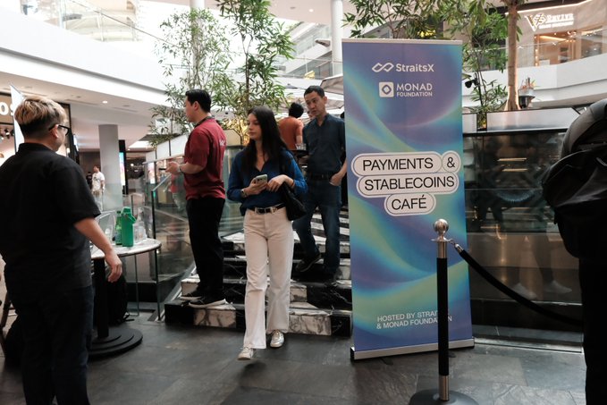 People gather near a banner reading 'PAYMENTS & STABLECOINS CAFÉ' hosted by StraitsX & Monad Foundation, in a shopping mall setting.