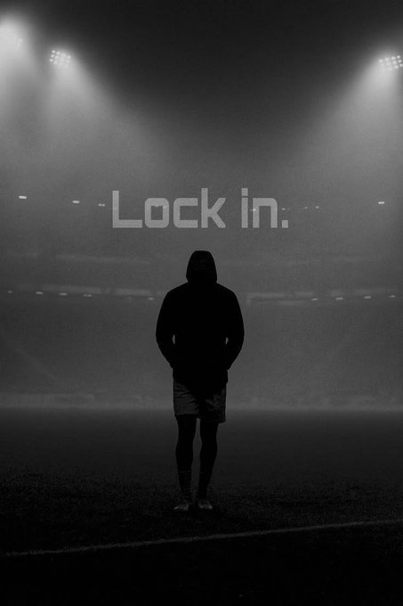 A black and white silhouette of a hooded figure stands on a sports field under bright stadium lights with the text 'Lock in.' in the background.