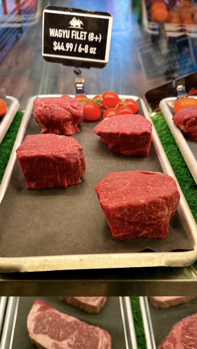 A butcher's display case showing thick cuts of Wagyu Filet (8+) labeled at $44.99 for 6-8 oz, garnished with cherry tomatoes.
