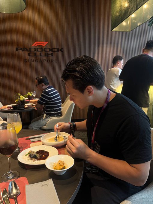 A man eats a meal at a Paddock Club Singapore hospitality suite, with other guests seated in the background.