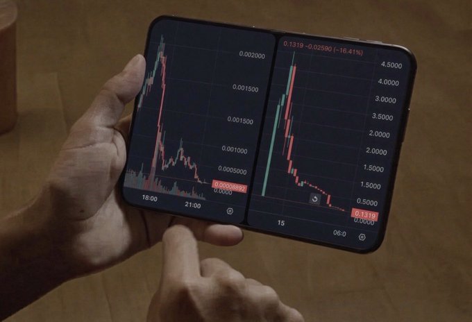 A person holds a foldable smartphone displaying two cryptocurrency trading charts with steep downward trends, showing numbers like '0.000892' and '0.1319'.