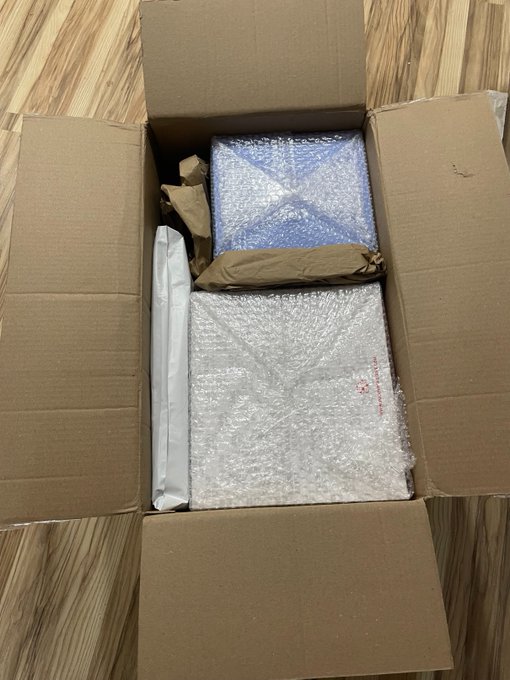 An opened cardboard box containing items wrapped in bubble wrap and a white shipping envelope.