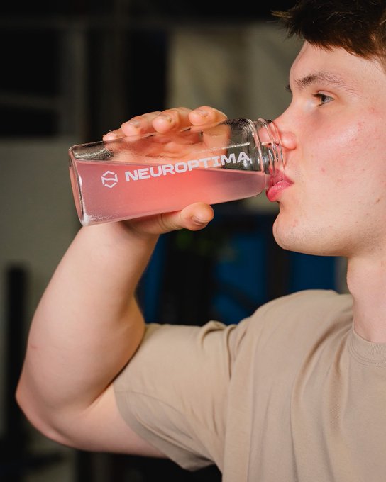 A young man drinks a pink beverage from a clear bottle labeled 'NEUROPTIMA' branded with a hexagonal logo.