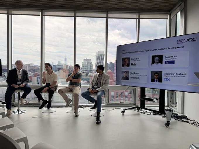 Four panelists—including representatives from XDC, Robot Ventures, Hivemind, and IBM—participate in a discussion titled "Panel: AI Agents on Blockchain: Hype, Hurdles, and What Actually Works," held in a modern high-rise venue overlooking a city skyline during the Fintech Meetup event.