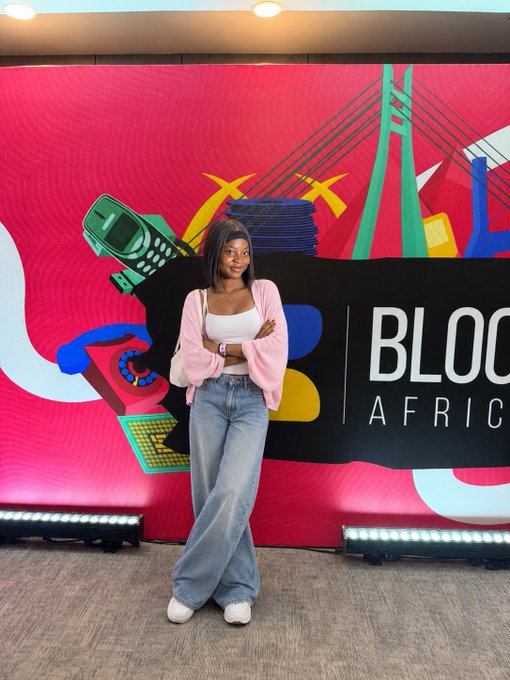 A woman poses with her arms crossed in front of a bright pink Blockfest Africa 2026 Day 1 backdrop featuring colorful event graphics and the visible text “BLOCK AFRICA.”