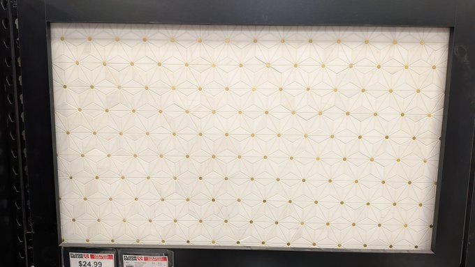 A retail display featuring a textured cream-colored geometric wallpaper panel framed in black, with a price tag showing $24.99.