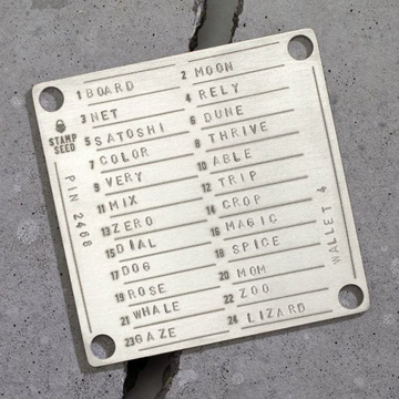 A metal plaque from the Stamp Seed PIN 2465, designed by Aallet, displays an engraved word list of 24 seed words including Board, Moon, Rely, Net, and Dune, used for cryptocurrency wallet recovery.