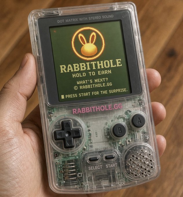 A hand holds a transparent handheld gaming console displaying a 'RABBITHOLD' game with a rabbit logo, advertising 'rabbithole.gg' and instructing to 'PRESS START FOR THE SURPRISE'.