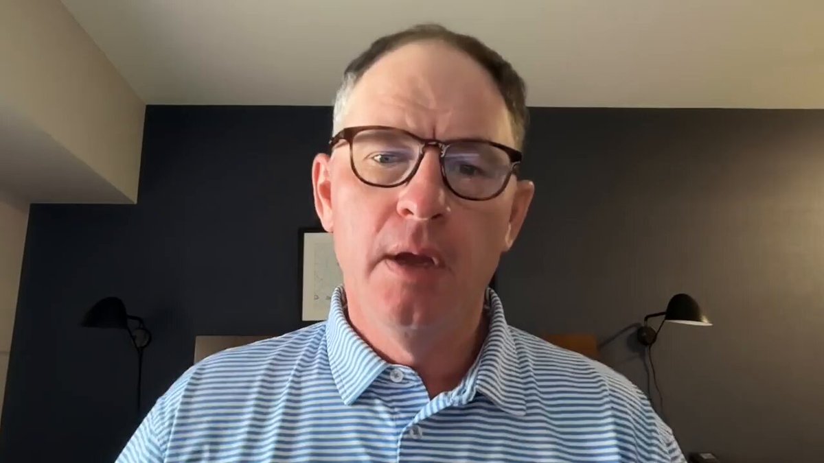 The image shows a man wearing glasses, standing against a wall with two lamps behind him. He appears to be looking at something off-camera or engaged in an activity that requires his attention. The caption of the image reads "XRP Times Up Watch The Full Youtube Video Here: youtu.be/-hv2U1Yxg2o". This suggests that the man might be watching a video related to cryptocurrency, specifically XRP, and is wearing glasses for better visibility or comfort while viewing it.