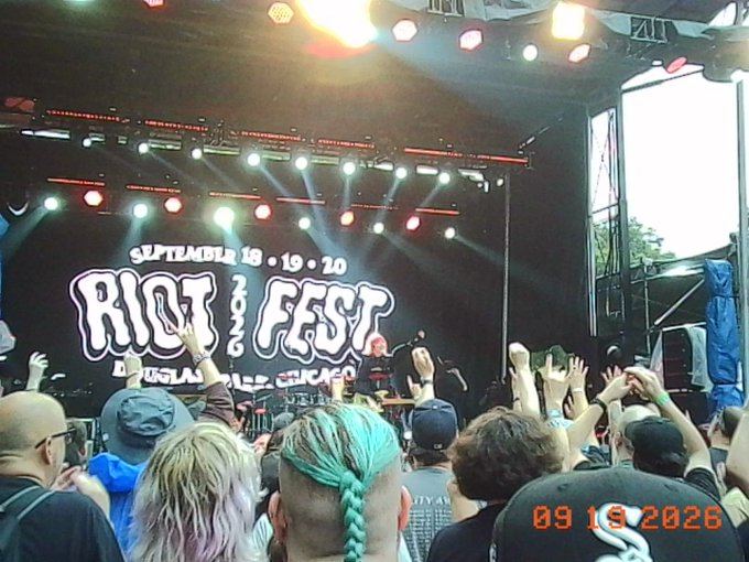 A concert crowd with raised hands facing the Riot Fest stage, which displays 'SEPTEMBER 19 • 19 • 20 DOUGLAS PARK CHICAGO' on the backdrop, dated 09 19 2026.