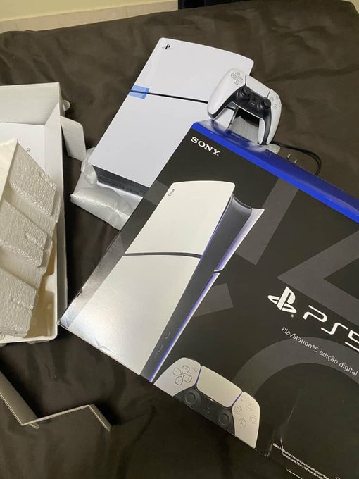 An unboxed PlayStation 5 Digital Edition console with its DualSense controller, box, and packaging materials laid out on a dark surface.