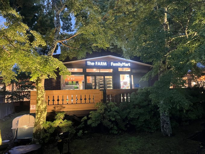 An evening photo of a small store labeled 'The FARM FamilyMart' nestled among trees, with lit windows and a wooden deck.