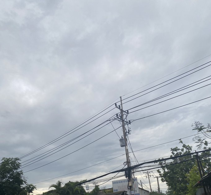 A utility pole with tangled power lines silhouetted against a cloudy gray sky.