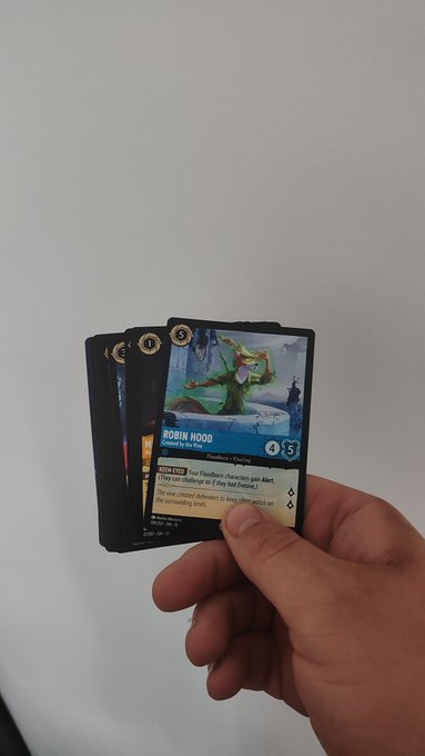 A hand holds a small fan of trading cards, with the top card displaying 'ROBIN HOOD' from a Fleurdelys + Pirates set, showing character artwork and game text.