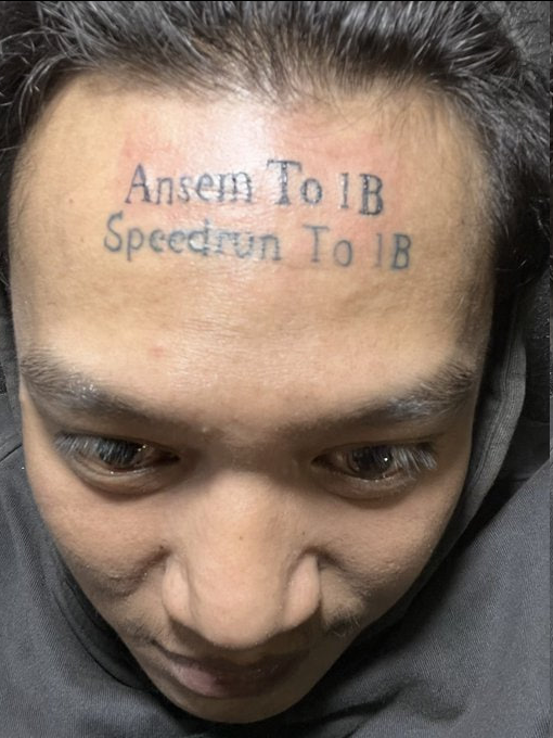 A close-up image of a person's forehead showing a tattoo with the text "Ansem To 1B" and "Speedrun To 1B" written on it. The image relates to a viral story about an Indonesian user who got this forehead tattoo to commemorate their goal of helping the cryptocurrency $ANSEM reach a $1 billion market cap, despite receiving no financial reward for the gesture.