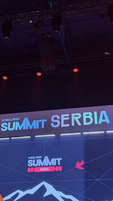 An illuminated stage setup displaying the 'SOLANA SUMMIT SERBIA' logo on a large screen under stage lighting.
