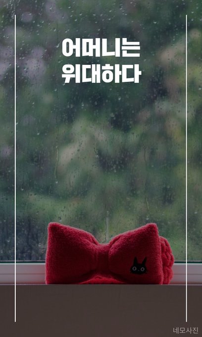 A red plush cat-shaped pillow with a bow sits on a windowsill against a rainy window background, with Korean text reading '어머니는 위대하다' (Mother is Great) and '네모사진' visible.