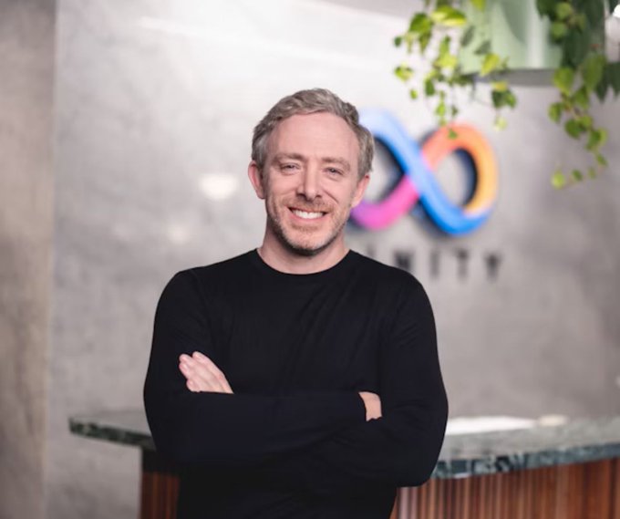 Dominic Williams, founder of Internet Computer ($ICP), stands smiling with his arms crossed in front of a colorful infinity-style logo. The image accompanies his claim that he exposed weaknesses in $NEAR’s confidential privacy claims.