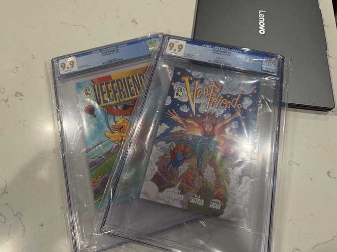 Two CGC-graded 9.9 comic books, 'Veefriends' and what appears to be 'Leerfienid', rest on a white surface next to a Lenovo laptop.
