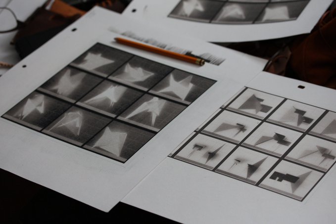 Several sheets of paper showing black and white photographic prints arranged in grids, with a yellow pencil resting on top of them.