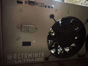 Close-up of an 'Octominer X8ULTRA Plus' cryptocurrency mining machine, showing its metal casing, control panel, and large black cooling fan.