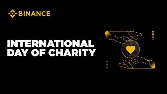 A Binance promotional graphic for 'INTERNATIONAL DAY OF CHARITY' featuring a gold illustration of two hands holding a heart.