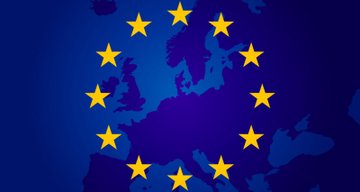 A European Union flag with its circle of gold stars on a blue background overlaying a map of Europe, symbolizing the EU's leadership in establishing comprehensive digital asset regulation that continues to attract crypto innovation and institutional investment.