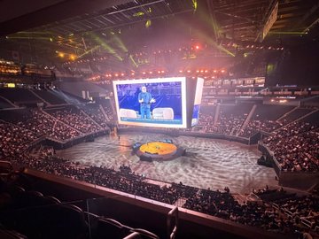 A packed arena features a large central screen displaying a digital ape character in a red-lit stage setup, with the accompanying post drawing a parallel to the Pier 17 BAYC party of 2022, both events showcasing the Bored Ape Yacht Club NFT imagery in elaborate entertainment venues.