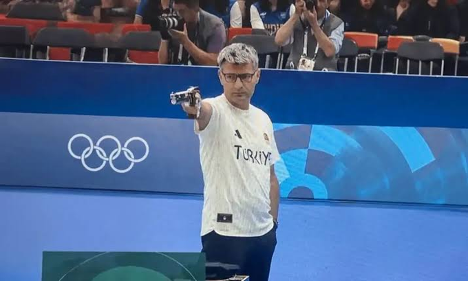 A Turkish shooter, identified by the "TÜRKİYE" jersey and Olympic rings backdrop, aims a pistol at the Paris 2024 Games. The image of a focused athlete taking aim visually mirrors the post's message about pursuing an independent path rather than following trends.