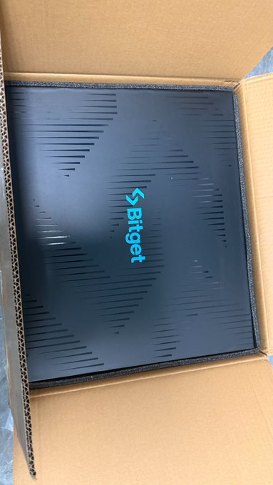 A black Bitget branded box with a stylized logo sits inside a cardboard shipping box.